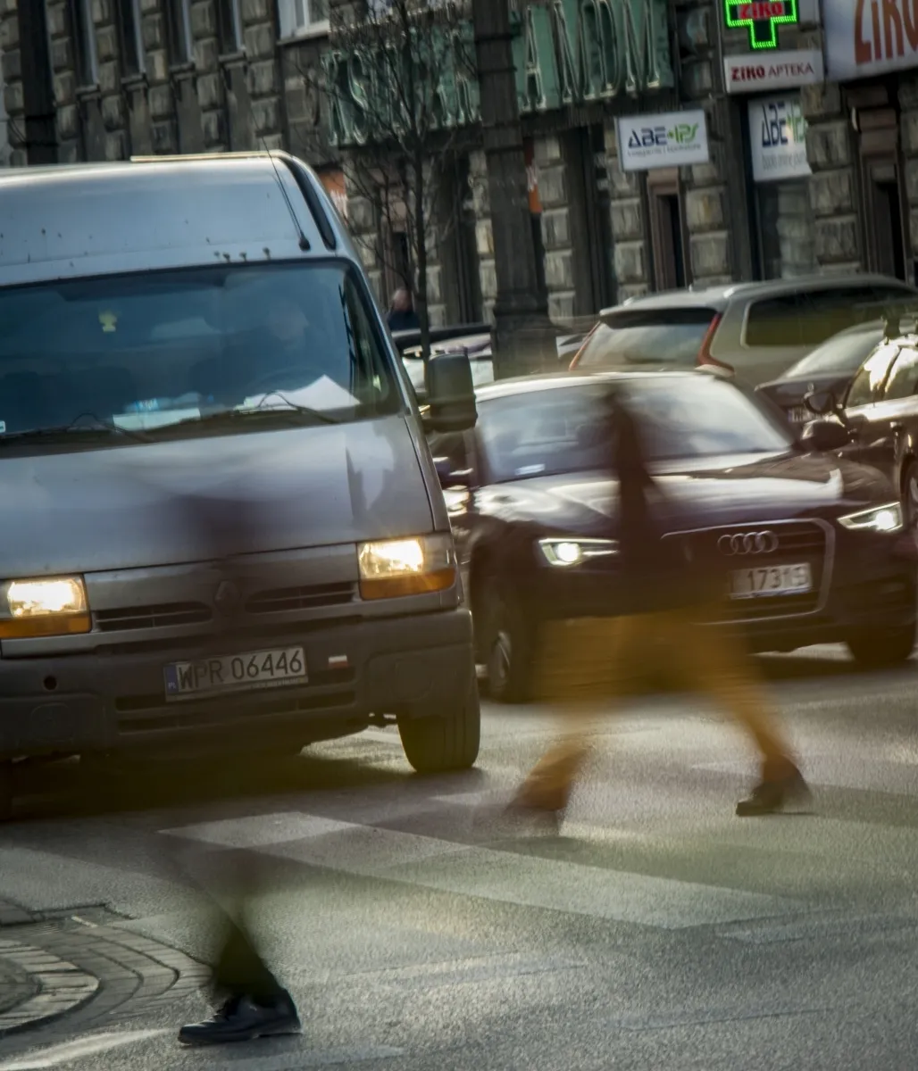 Blurred pedestrian crossing in front of cars and a dark van